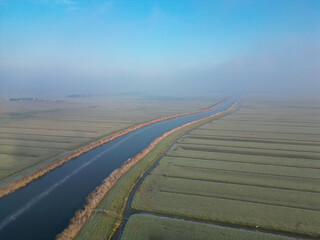 Winter landscape with a frozen river seen from above. A vast plain full of Dutch water canals seen from the drone early in the morning in Netherlands