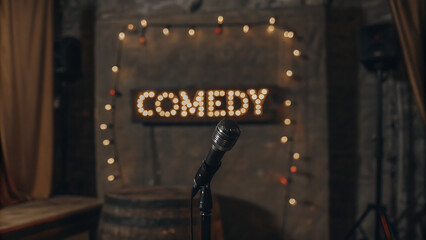 A microphone on a stand in front of a comedy sign with warm lights. The background is a rustic, dimly lit stage setting. Perfect for comedy shows.