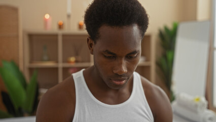 Young man in spa center wearing white tank top with candles and plants in background