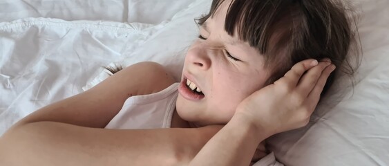 Little girl child screams in pain in bed with hand pressed to ear