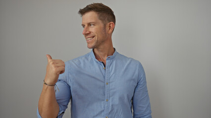 Young man smiling confidently while gesturing with thumb on isolated white background in casual...