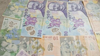 Various romanian banknotes of different denominations including 1 leu, 10 lei, and 100 lei, are laid out flat, showcasing the colorful designs and historical figures.