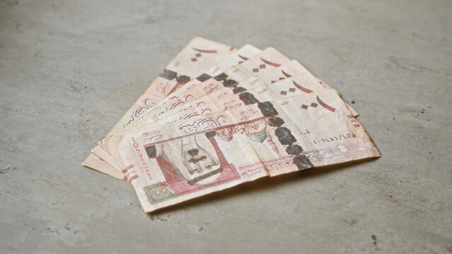 Saudi riyals banknotes spread on a concrete surface, representing middle eastern currency in a simple, neutral setting.
