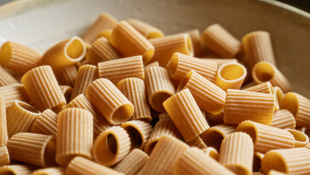 Close-up of uncooked pasta with a ridged texture in a shallow bowl, highlighting the intricate details of the cylindrical shapes.