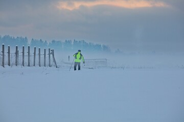 Cross-country skier skiing through winter field with clouds in the sky.