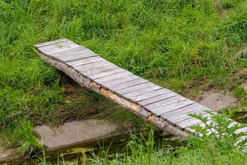  Drewniany most z desek i pali nad strumieniem ze wzmocnionym korytem. Bujne, soczyste łąki , przez które przepływa mały strumień z małym mostkiem nad jego brzegami w sierpniowy poranek. © Grzegorz