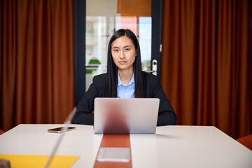 Asian woman sits at head of conference table in meeting room