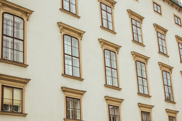 Fototapeta premium Vienna, Austria - May 12, 2019: Ancient architecture of residential buildings. Windows of beautiful palace with Barocco ornaments, closeup photo. Wall exterior with parts of yellow windows.