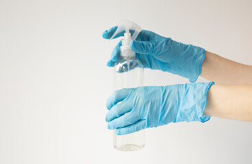 Fototapeta premium Female hands in protective rubber medical gloves of blue color, hold a bottle of antiseptic. on white background isolate.