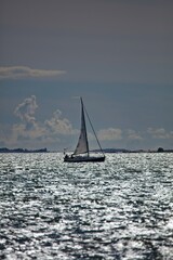 Fototapeta premium Sailboat silhouette on glistening sea in summer.