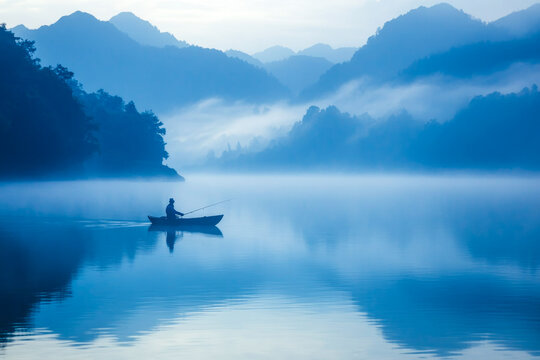 Solitary fishing at dawn on foggy lake with mountain views