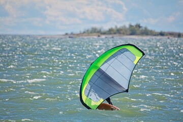 Man is wing foiling using handheld inflatable wing and hydrofoil surfboard in sea in summer. Rider on a wind wing board, surfs the waves.
