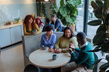Diverse business team enjoying coffee break, discussing work in modern office cafeteria