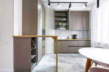 Modern kitchen in a small cozy contemporary studio apartment. Table and chairs in the foreground. Built in household appliance