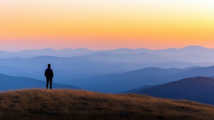 Obraz premium Person standing on hilltop watching gradient sunset over distant mountains