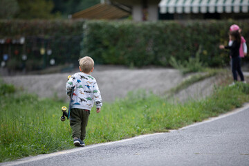 beautiful little and friendly blond boy playing on his skateboard