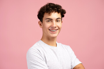 Smiling, handsome teen boy with braces wearing white t shirt, posing isolated on pink background