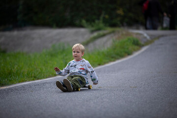 beautiful little and friendly blond boy playing on his skateboard