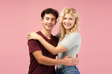 Fototapeta premium Happy boyfriend and girlfriend, couple embracing together, standing isolated on pink background