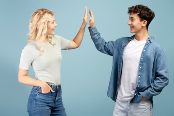 Happy, smiling teenagers, boy and girl giving high five, standing isolated on blue background