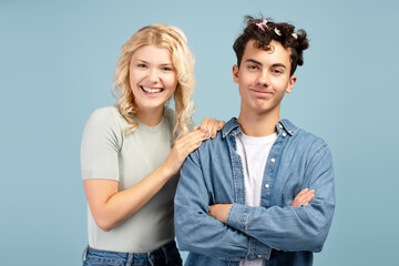 Attractive couple, smiling girl doing hairstyle to handsome boy isolated on blue background