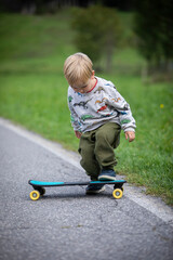beautiful little and friendly blond boy playing on his skateboard