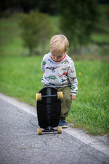 beautiful little and friendly blond boy playing on his skateboard