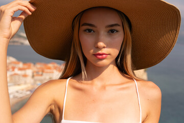 A woman in a straw hat stands in front of the sea