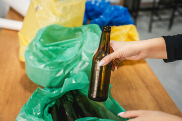 Unknown woman recycle at home glass bottle in the green plastic bag