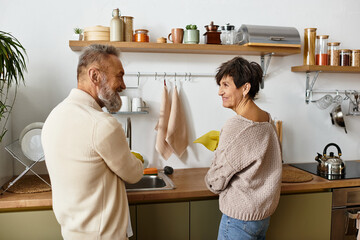 A happy senior couple enjoys washing dishes together in their cozy kitchen.