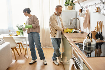 A mature couple shares joyful moments while washing dishes in their warm kitchen.