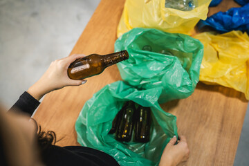 Unknown woman recycle at home glass bottle in the green plastic bag