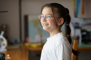Little beautiful teenage girl in glasses with a hairstyle. Blurred children's room in the...