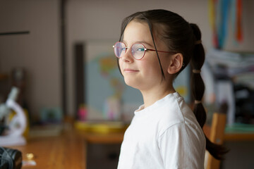Little beautiful teenage girl in glasses with a hairstyle. Blurred children's room in the...