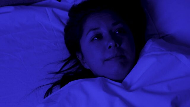 Young woman wakes up after a nightmare, horrible dream, blue night light
