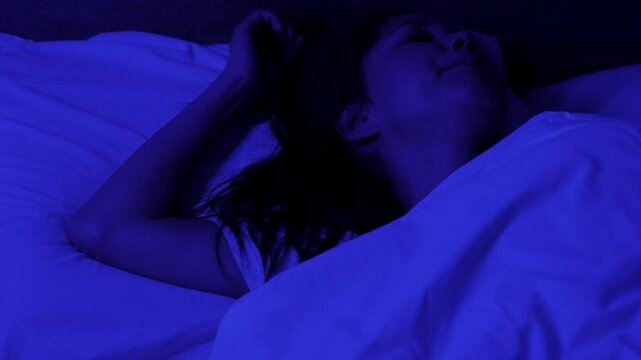 Young woman wakes up after a nightmare, horrible dream, blue night light