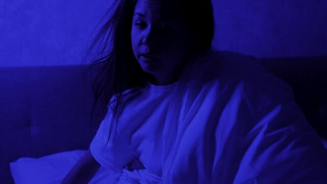 Young woman wakes up after a nightmare, horrible dream, blue night light