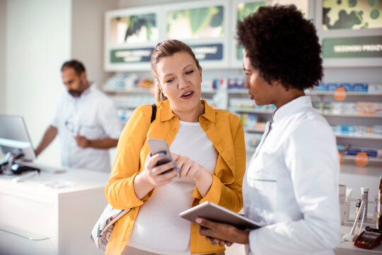 Female pharmacist helping pregnant woman in drug store