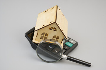 Black calculator and wooden house under magnifying glass. Review price of house and housing concept.