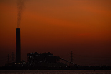Obraz premium Night of Industrial skyline with smokestack emissions shows urban pollution, climate change, and environmental impact. The silhouette emphasizes air pollution and the need for sustainable solutions.
