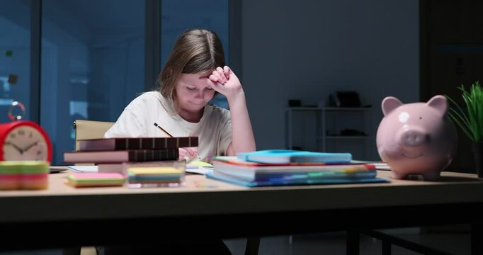 Schoolgirl writes down complicated homework in paper notebook. Concentrated girl sits at desk and writes answers to math problems. Slow motion