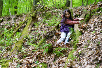 A small beautiful smiling long-haired dark-haired girl in glasses and a vest goes down in the forest