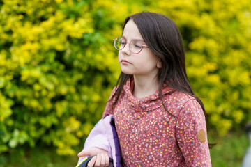 Little beautiful sad long dark haired girl with glasses on blurry green background