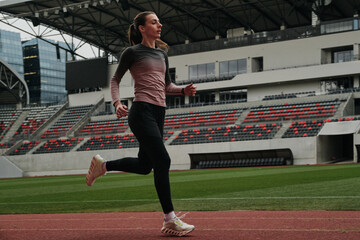 Female athlete running on a track at a modern stadium.  Determined runner in action, showcasing...