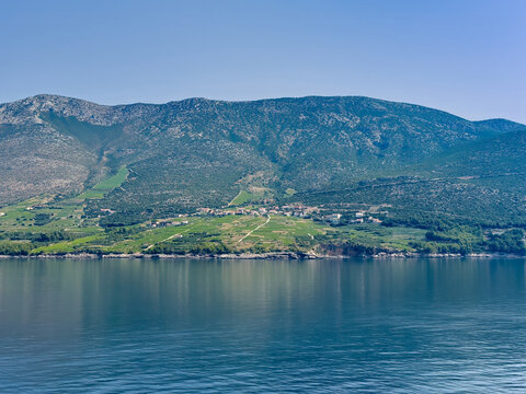 Korcula, Croatia - June 30, 2024: Postup Vineyards on mainland opposite, north of the island. Long large flank of mountains with green vineyards close to the Adriatic. Small settlement with red roofed