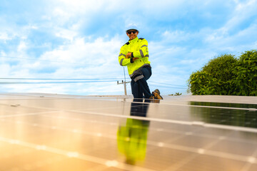 A technician in safety gear inspects solar panels on a metal rooftop, holding a tool. The scene...