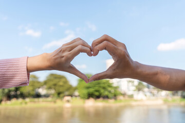 Affectionate heart gesture between two hands outdoor park human connection natural setting close-up perspective love concept