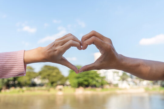 Affectionate heart gesture between two hands outdoor park human connection natural setting close-up perspective love concept