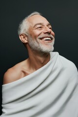 Obraz premium A man with a white towel draped over his shoulders is smiling. Concept of warmth and happiness, as the man is enjoying a relaxing moment. The white towel adds a touch of elegance