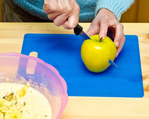 Making cookies. The cook has added walnut and starts to cut apple.